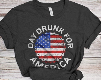 May include: A dark grey t-shirt with a white distressed circle design featuring an American flag and the text "Day Drunk For America".