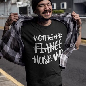 May include: A black t-shirt with white text that reads "Boyfriend Fiance Husband".