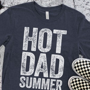 May include: A dark blue t-shirt with a white distressed graphic that reads "HOT DAD SUMMER".