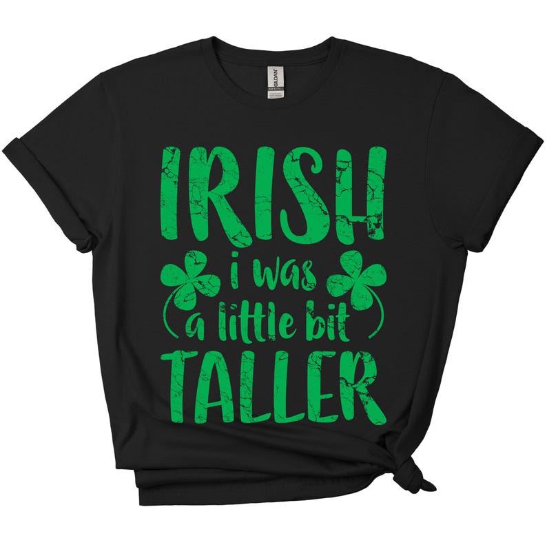 K&ouml;nnte beinhalten: Schwarzes T-Shirt mit einem gr&uuml;nen, abgenutzten Aufdruck, der "Irish I was a little bit taller" lautet, mit Kleeblatt-Designs auf beiden Seiten des Textes.