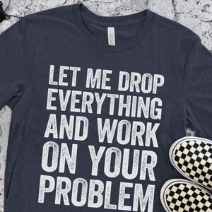 May include: A navy blue t-shirt with white text that reads "Let me drop everything and work on your problem".