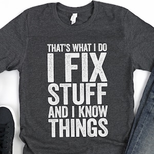 May include: A dark gray t-shirt with the text "That's what I do I fix stuff and I know things" printed in white.