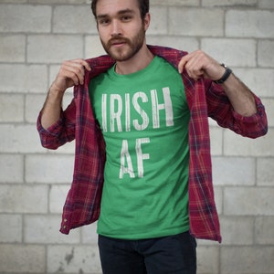 May include: A green t-shirt with white text that reads "IRISH AF". The person is wearing a red and black plaid shirt over the t-shirt.