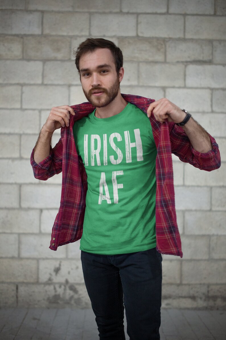 May include: A green t-shirt with white text that reads "IRISH AF". The person is wearing a red and black plaid shirt over the t-shirt.