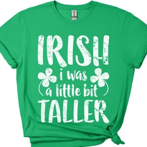 K&ouml;nnte beinhalten: Gr&uuml;nes T-Shirt mit wei&szlig;em Text, der "Irish I was a little bit taller" lautet, mit Kleeblatt-Designs auf beiden Seiten des Textes.