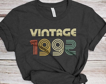 May include: A dark gray t-shirt with the text "Vintage 1992" in a retro font with colorful stripes.