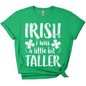 K&ouml;nnte beinhalten: Gr&uuml;nes T-Shirt mit wei&szlig;em Text, der "Irish I was a little bit taller" lautet, mit Kleeblatt-Grafiken.