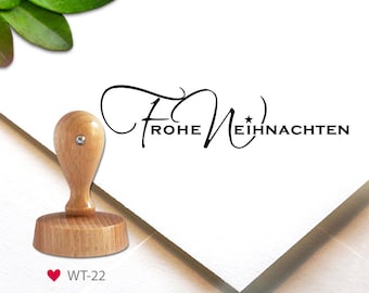 May include: Wooden stamp with the text "Frohe Weihnachten" in a cursive font. The stamp is on a white background and has a small heart with the text "WT-22" below it.
