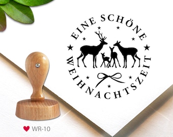 May include: A round black and white rubber stamp with a deer family and the text "Eine schöne Weihnachtszeit" in a circle. The stamp is on a white background.