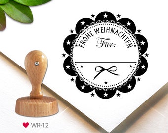 May include: A black and white rubber stamp with a circular design. The stamp features a decorative border with stars and a lace pattern. The text "Frohe Weihnachten" is written in a circle around the center of the stamp. The text "Für:" is written in the center of the stamp.