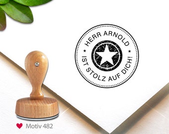 May include: A wooden stamp with a round, black ink imprint that reads "HERR ARNOLD IST STOLZ AUF DICH!" around a star. The stamp has a light-colored wooden handle and base. The image also includes the text "Motiv 482".
