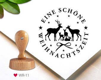 May include: A round wooden stamp with a black ink design of a family of deer with the text "Eine schöne Weihnachtszeit" around the outside.