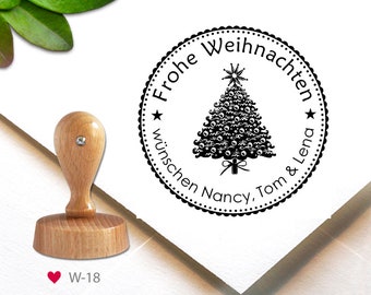 May include: A black and white round rubber stamp with a Christmas tree design. The text reads "Frohe Weihnachten wünschen Nancy, Tom & Lena".