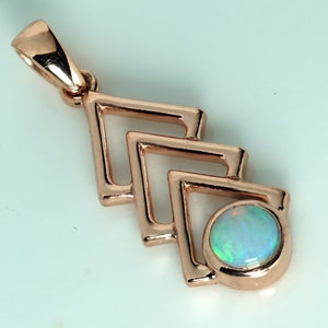 Może przedstawiać: Zawieszka z różowego złota z geometrycznym wzorem trzech otwartych kwadratów i okrągłą oprawą. Oprawa zawiera okrągły opal z niebieskimi, zielonymi i białymi iryzacjami. Zawieszka ma krawat do łańcuszka.