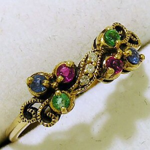 Op de afbeelding: Een goudkleurige ring met kleurrijke edelstenen. De ring is versierd met rode, groene, blauwe en heldere stenen, gezet in een decoratief ontwerp. De band is eenvoudig en goudkleurig. Een uniek sieraad.