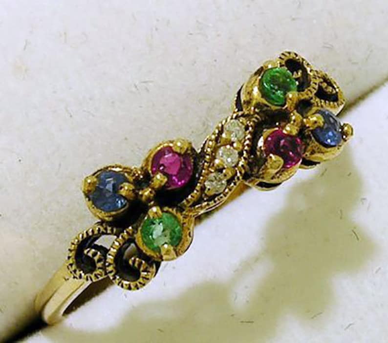 Op de afbeelding: Een goudkleurige ring met kleurrijke edelstenen. De ring is versierd met rode, groene, blauwe en heldere stenen, gezet in een decoratief ontwerp. De band is eenvoudig en goudkleurig. Een uniek sieraad.
