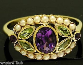 Op de afbeelding: Een gouden ring met een ovale, dieppaarse amethist middensteen, omringd door kleine parels en groene en paarse accentstenen. De ring heeft een gedetailleerd, sierlijk ontwerp, dat een vintage of antieke stijl suggereert.