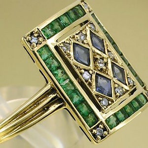 Pu&ograve; includere: Anello in oro con una faccia rettangolare decorata con smeraldi, pietre preziose blu e piccoli diamanti. Il gambo dell'anello &egrave; diviso in tre sezioni parallele. Gioiello di lusso.