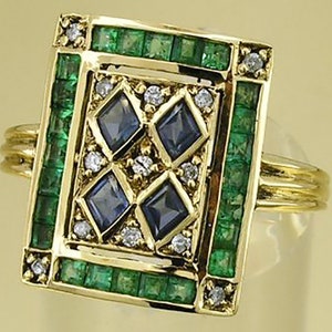 Pu&ograve; includere: Un anello d'oro con una faccia rettangolare ornata di smeraldi e zaffiri. La faccia &egrave; bordata da smeraldi e contiene quattro zaffiri quadrati, circondati da piccoli diamanti. L'anello ha una fascia d'oro a pi&ugrave; bande.