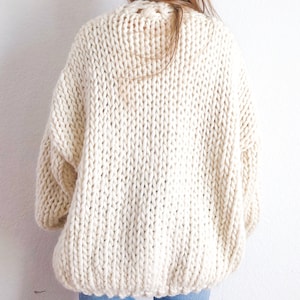 May include: A cream-coloured chunky knit cardigan with a relaxed fit. The cardigan is made from a thick yarn and has a loose, oversized style.