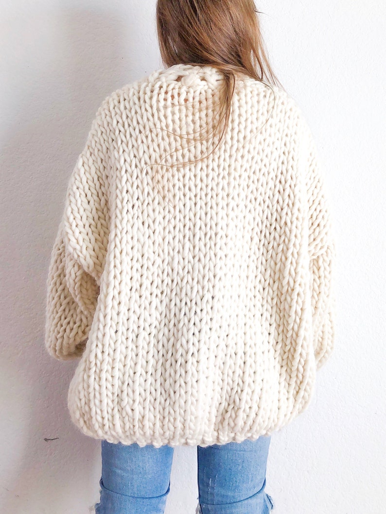 May include: A cream-coloured chunky knit cardigan with a relaxed fit. The cardigan is made from a thick yarn and has a loose, oversized style.