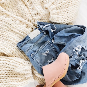 May include: A white chunky knit cardigan, blue denim jeans with distressing, and a pair of pink leather clogs with wooden soles.