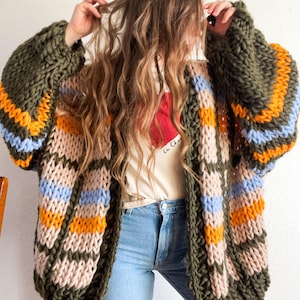 May include: A chunky knit cardigan with a striped pattern in shades of green, orange, pink, and blue. The cardigan has a relaxed fit and a long, open front.