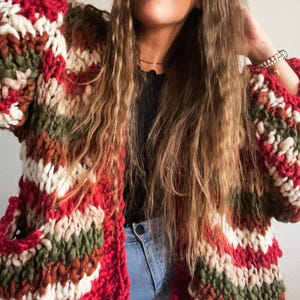 Peut inclure: Un cardigan en tricot épais avec un motif rayé audacieux de rouge, blanc, vert et marron. Le pull surdimensionné présente de grandes manches et des poches. Le fil a un aspect texturé, créant une esthétique chaleureuse et confortable.