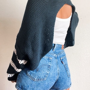 Puede incluir: Un suéter de punto azul oscuro con la espalda recortada y mangas a rayas blancas. El suéter se lleva sobre un top blanco sin mangas y se combina con pantalones cortos de mezclilla.