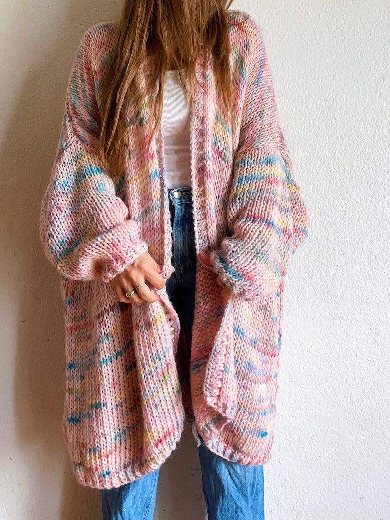Op de afbeelding: Een lange, oversized cardigan in een roze en veelkleurige garen met een losse brei. De cardigan heeft een V-hals en lange mouwen.