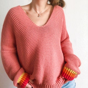 May include: A coral pink knitted sweater with a v-neck and colorful stripes on the cuffs.
