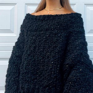 May include: A black off-the-shoulder sweater with a chunky knit texture and gold flecks throughout.