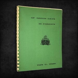 May include: A green book with the title "Of Green Days in Forests" and the author's name "Dale C. Olsen". The book has a spine with a spiral binding.