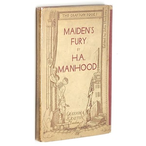 Puede incluir: Una cubierta de libro vintage con lomo rojo y cubierta delantera beige. El título es "MAIDEN'S FURY" por H.A. MANHOOD. La cubierta presenta una ilustración en blanco y negro de una mujer con un vestido de pie frente a un edificio.