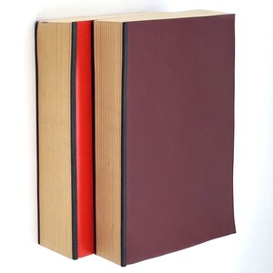 Puede incluir: Dos libros de tapa dura uno al lado del otro. El libro de la izquierda tiene una cubierta de color beige con una lomo rojo. El libro de la derecha tiene una cubierta de color rojo oscuro con una lomo negro.