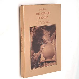 Può includere: Una copertina di libro con sfondo marrone e una foto di una persona che lavora al tornio. Il titolo del libro è "The Mud-Pie Dilemma: A Master Potter's Struggle to Make Art and Ends Meet" di John Nance.