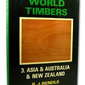 May include: A hardback book titled World Timbers 3. Asia & Australia & New Zealand by B.J. Rendle. The black cover features a central rectangular inset showing a light brown wood grain pattern. The title is in green and yellow text.