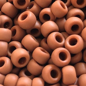 Pode incluir: Um monte de contas redondas de cor terracota. Cada conta tem uma forma cilíndrica com um grande buraco que atravessa o centro. As contas são lisas e de cor uniforme, criando uma aparência uniforme.
