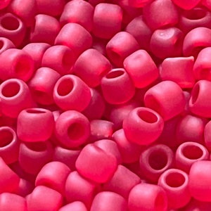 May include: A close-up view of a large quantity of small, opaque, pink beads. The beads are round and have a smooth, slightly glossy finish.