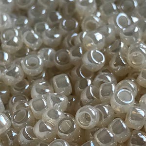 May include: A close-up of a pile of small, round, iridescent white beads. The beads are translucent and have a slight shimmer to them.