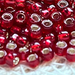 Peut inclure: Un grand tas de petites perles de verre rouges avec des capuchons en métal argenté. Les perles sont rondes et ont une surface brillante et réfléchissante.