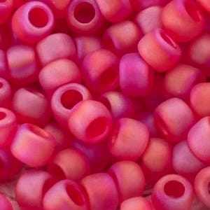May include: A close-up of a pile of small, round, pink and orange beads. The beads have a frosted finish and are arranged in a random pattern.