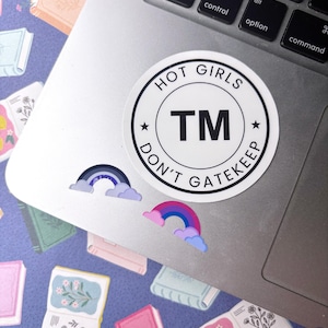 May include: A circular white sticker with black text reading HOT GIRLS DON'T GATEKEEP and TM in the center. Below it are two smaller stickers: one with a dark blue and purple rainbow with light purple clouds, and one with a pink, blue, and purple rainbow.
