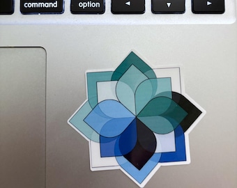 May include: A sticker with a geometric floral design. The sticker features overlapping petals in shades of blue, teal, and black, set against a white square border. The sticker is on a silver surface.