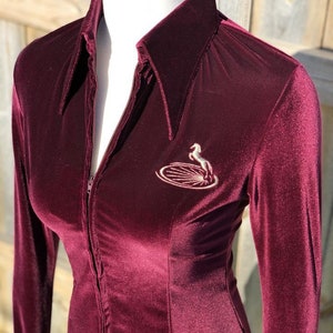May include: A maroon velvet long-sleeved shirt with a zipper closure and a horse logo embroidered on the front.