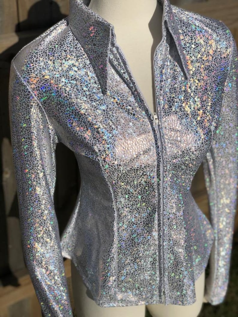 Op de afbeelding: Een zilveren, iriserende blouse met lange mouwen en een ritssluiting. De blouse heeft een subtiel patroon van kleine, iriserende vierkantjes.