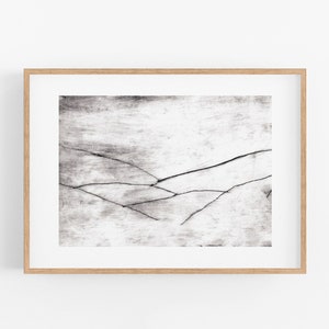 Op de afbeelding: Een zwart-witte abstracte kunstprint met een minimalistisch ontwerp met dunne lijnen die een landschapsachtig beeld creëren. De print is ingelijst in een naturel houten lijst.