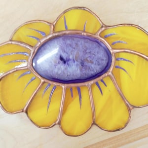 May include: A stained glass flower with yellow petals and a purple center. The petals have blue accents and are outlined with copper. The flower is a decorative piece, likely for display.