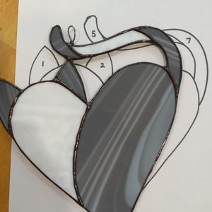 May include: A stained glass pattern of a kitty cat in the shape of a heart. The pattern is numbered 1, 2, 5, and 7. The glass is gray and white.