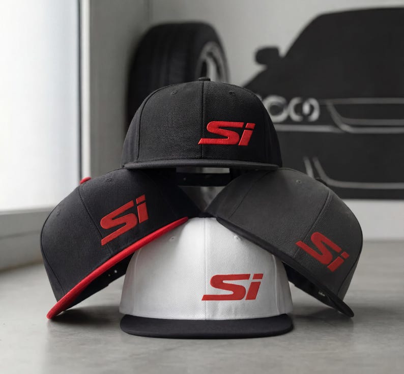 May include: A stack of flat-brimmed baseball caps in black, gray, and white. Each cap features the embroidered letters "Si" in red. One cap has a red brim. The caps are stacked on a light gray surface.